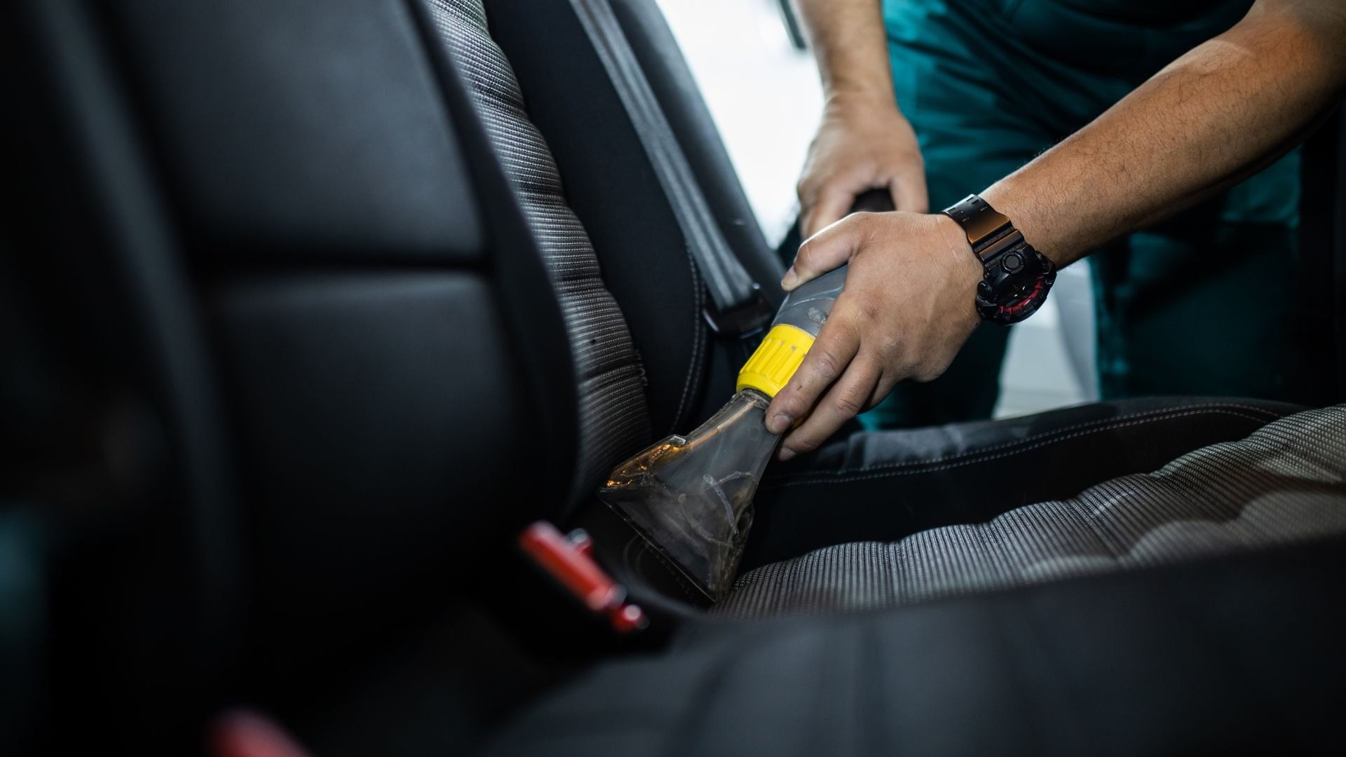 Person using vacuum cleaner to clean car interior seat upholstery