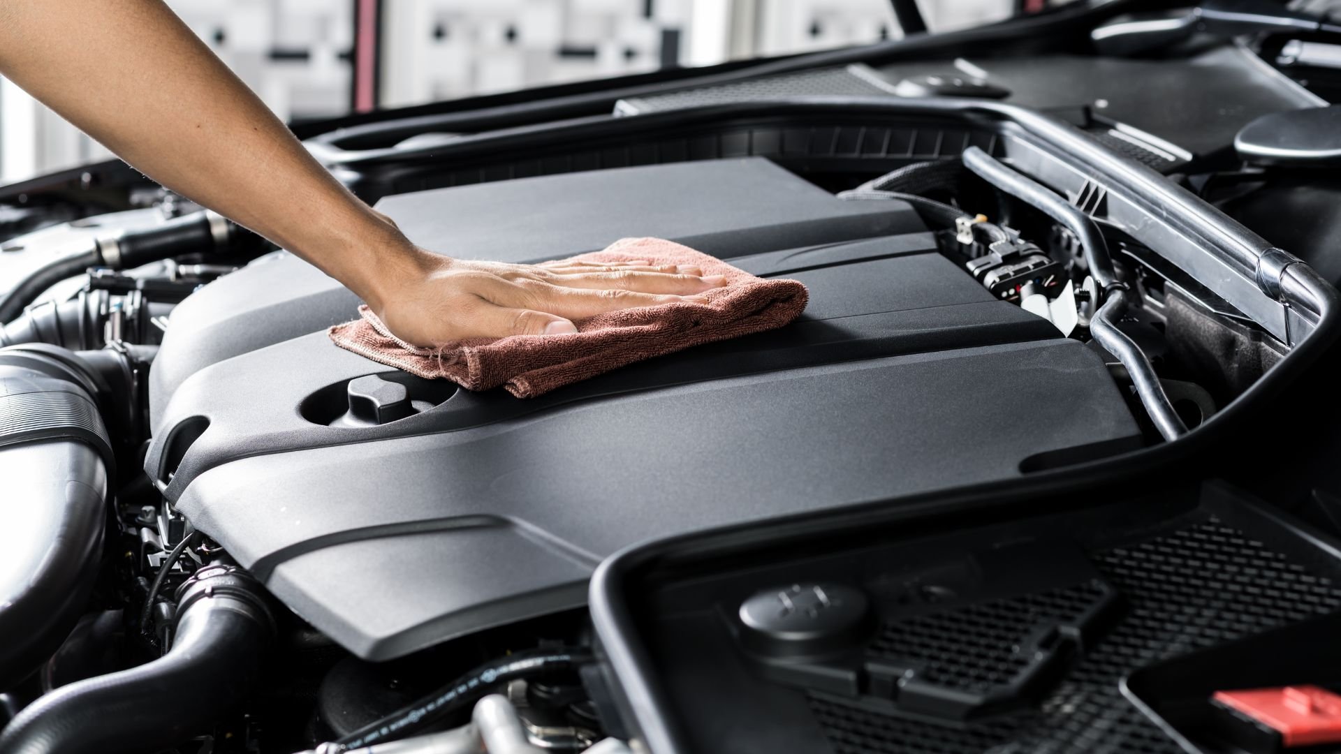 Hand wiping clean car engine with microfiber cloth in auto workshop